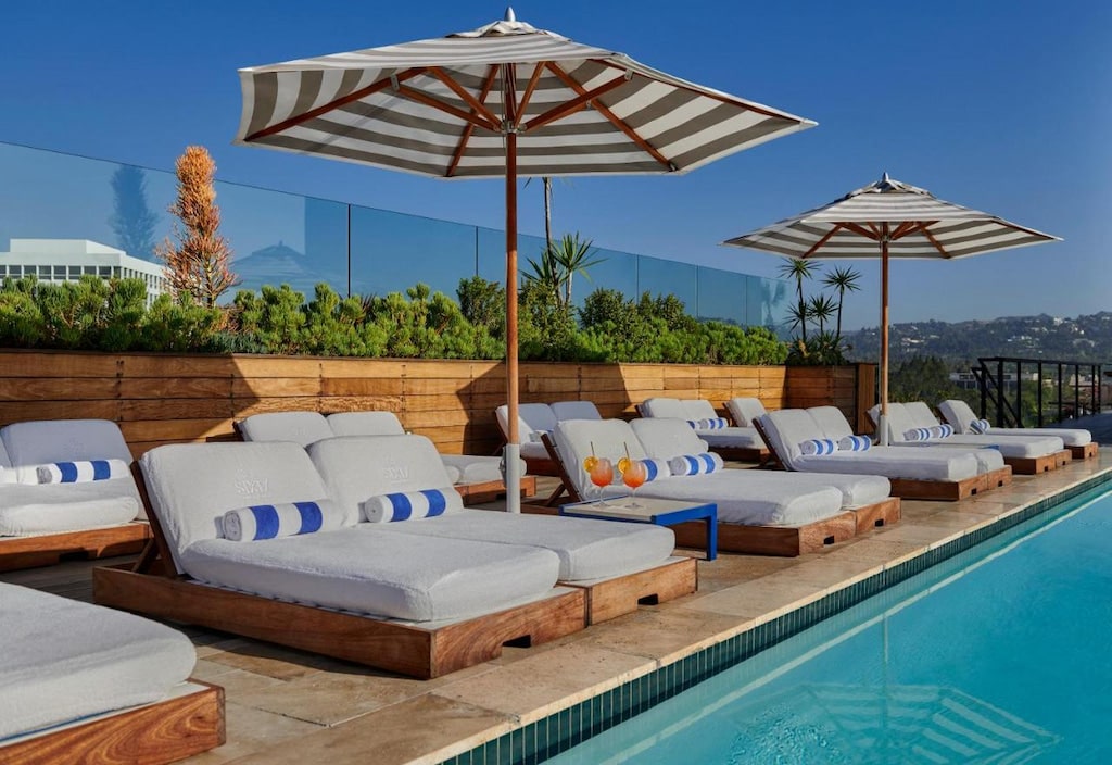 sun loungers poolside with striped umbrellas and green shrubbery at this cool boutique Beverly Hills hotel