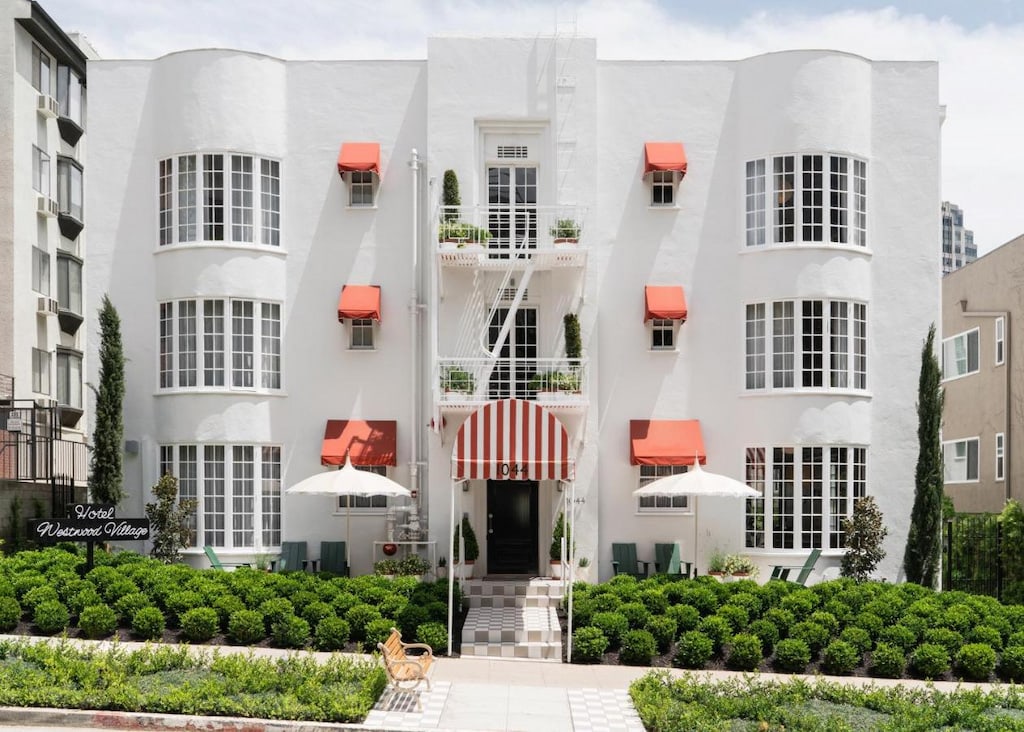 whitewashed 5 star Beverly Hills hotel facade with red window awnings and green shrubbery