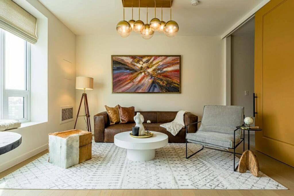 boutique styled luxury condo in downtown Los Angeles with brown leather couch, grey chair, round white coffee table and mid-century round chandelier