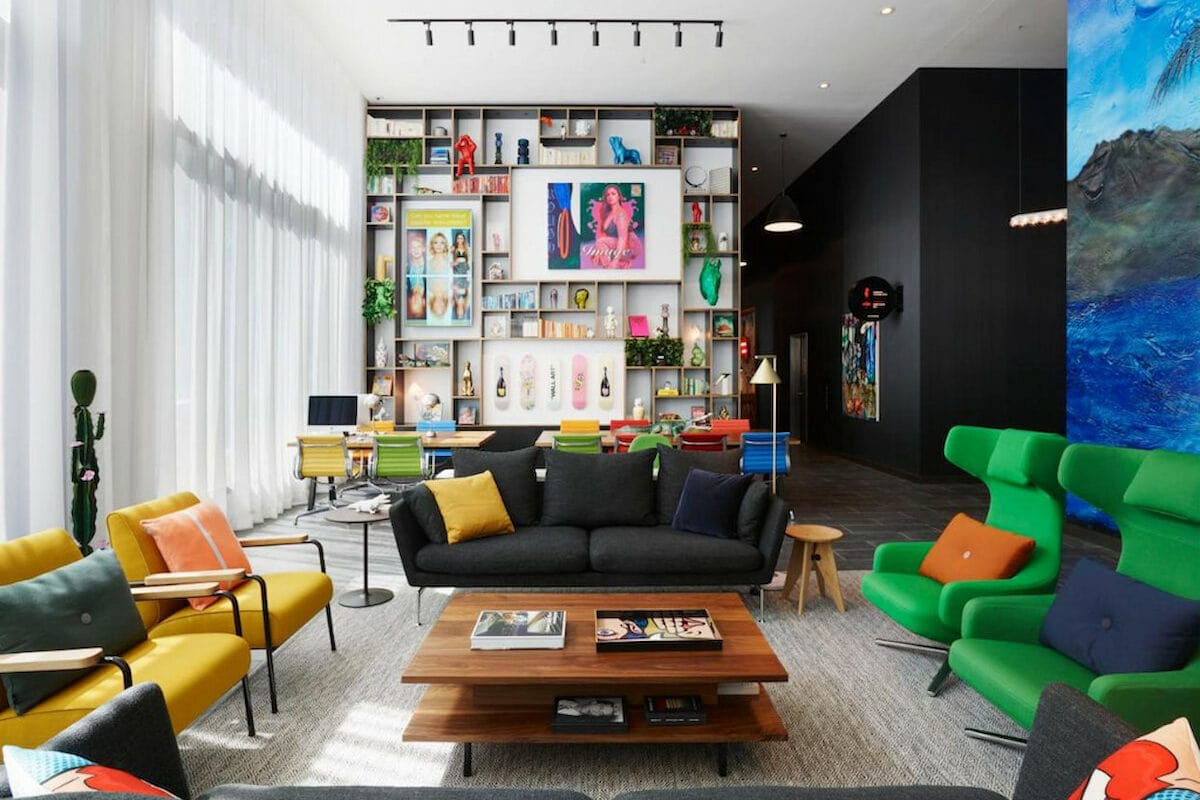 primary coloured furniture in large hotel welcome room with tall ceiling and eclectic bookshelf at a downtown LA boutique hotel