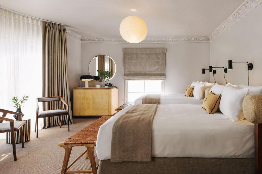 earthy toned boutique Los Angeles hotel with two plush beds, wood dresser and two arm chairs with round light fixture