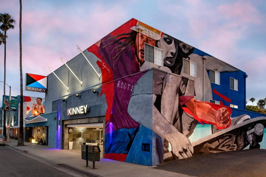 urban mural with skateboarders painted in purple, red, grey and blue on the side of a box shaped trendy LA hotel in Venice Beach