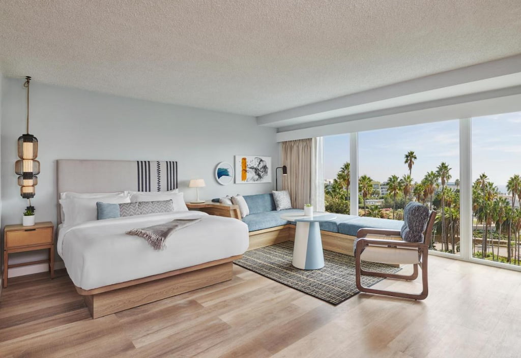 A spacious Santa Monica hotel bedroom with a bed and an L-shaped sofa by the corner of the room.