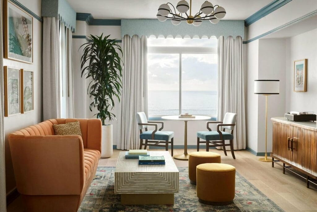 A chic hotel in Santa Monica California with an orange couch, tables, stools and cabinet.