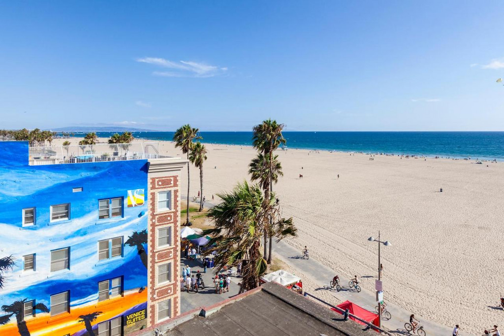 Overview of a Venice Beach hotel with people on bicycles in front with the ocean in the distance.
