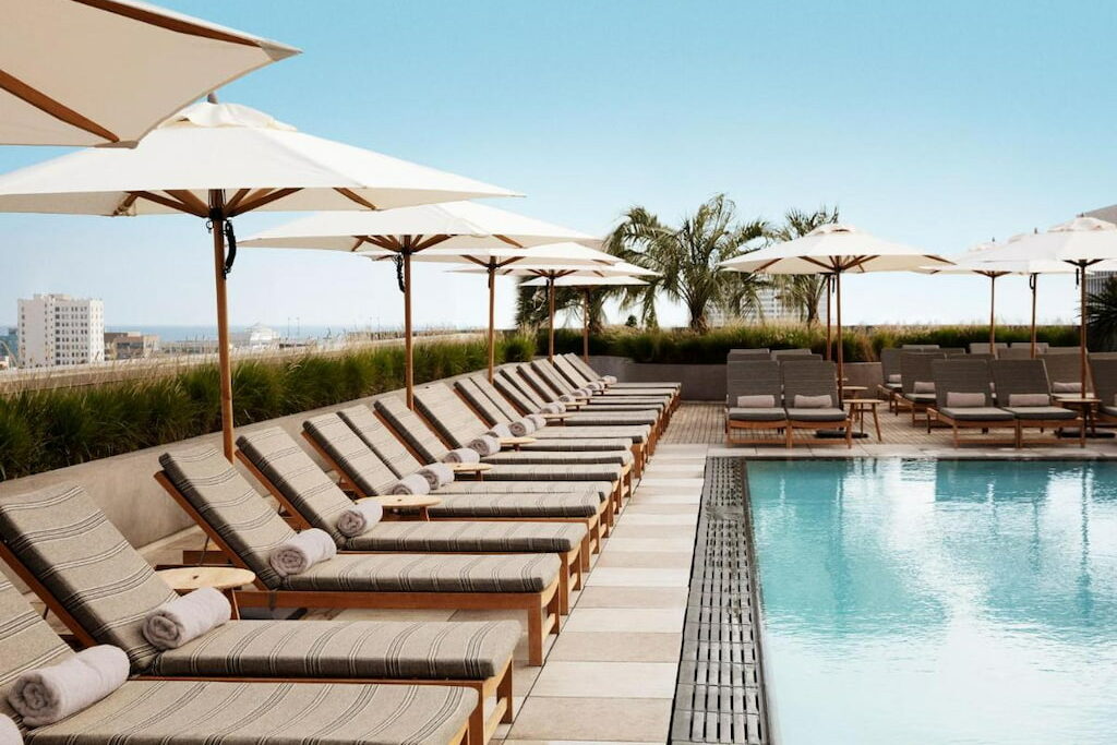 A rectangular outdoor pool surrounded by loungers and white umbrellas under a clear sky.