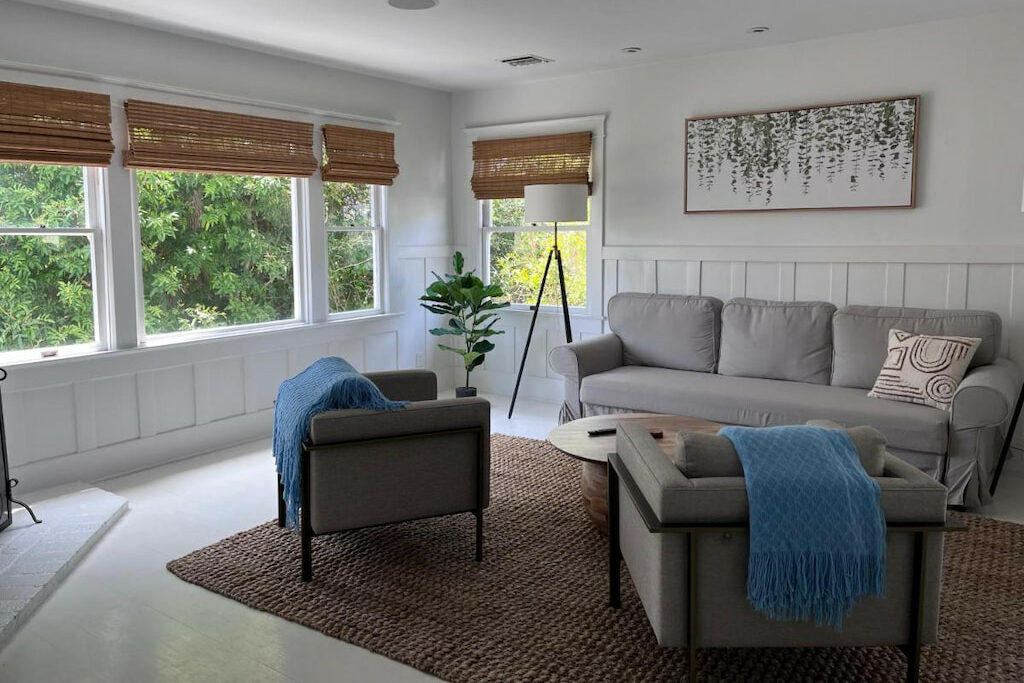 A spacious living room area with a gray sofa set with blue linens near the window with blinds.