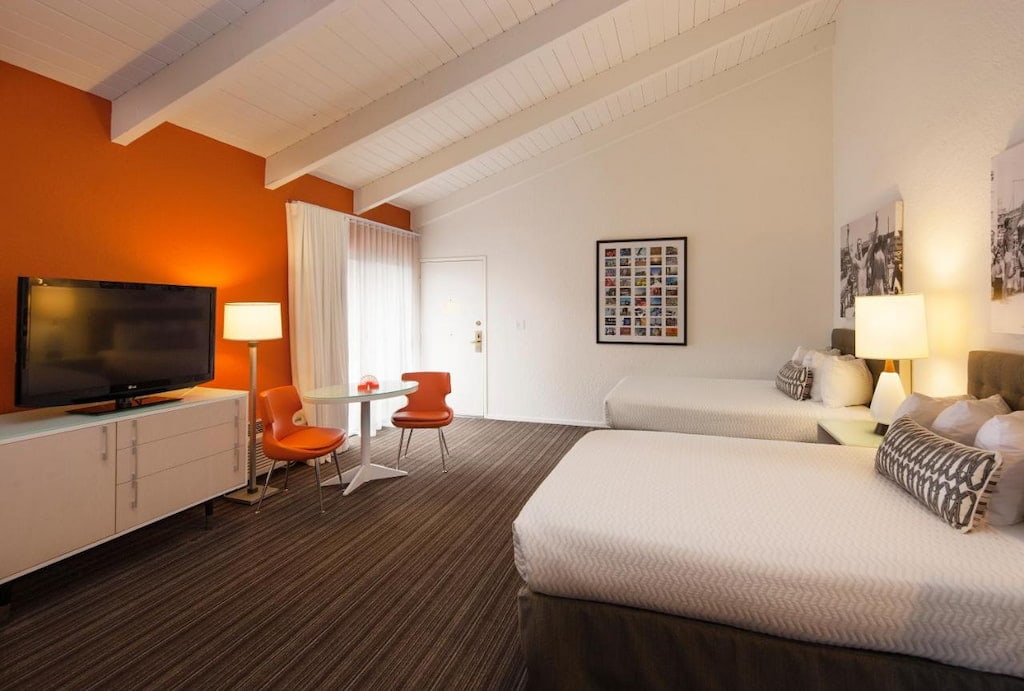 A modern room at a Venice Beach boutique hotel with orange walls and two beds with white sheets.