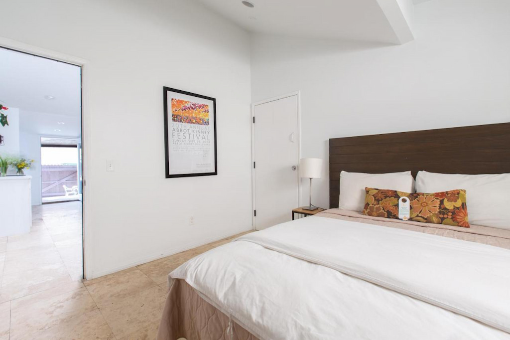 A minimalist room with a comfy bed with white sheets and a painting.