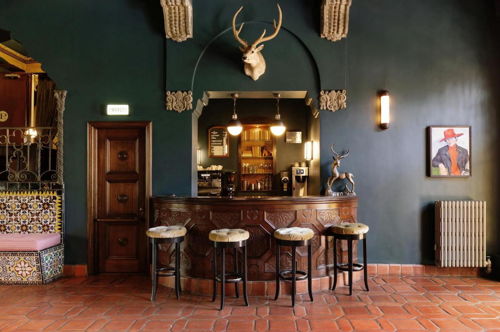A small bar with stool chairs below the hanging head of a deer.