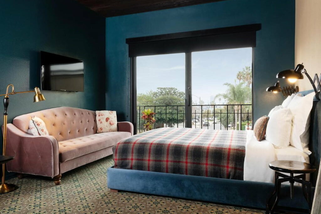 A modern style hotel room with a pink couch near the bed by the window and dark blue wallpaper.