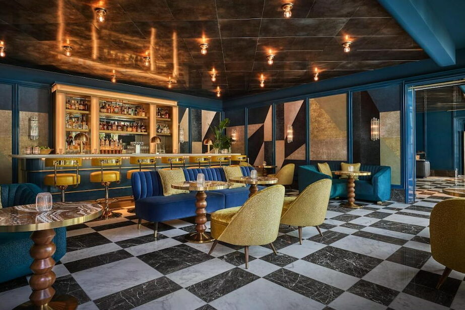 A sophisticated bar at a cool hotel in West Hollywood with blue and gold accent design and a bar filled with variety of wine bottles.