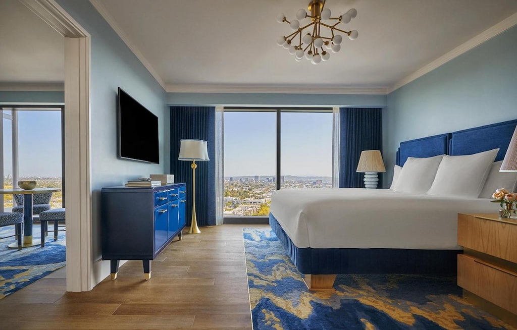 A boutique hotel in West Hollywood with royal blue colors, with a console table, cozy bed, side tables, flat screen TV and ceiling-to-floor windows.