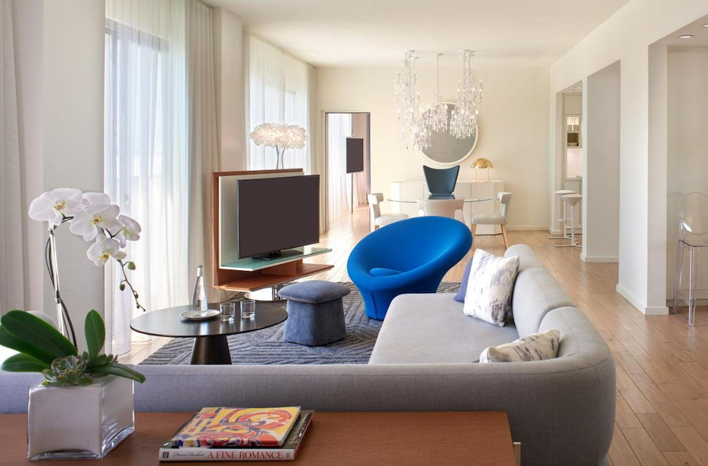 A spacious stylish living room with a blue accent chair in the middle near the flat-screen TV, grey soda by the window.