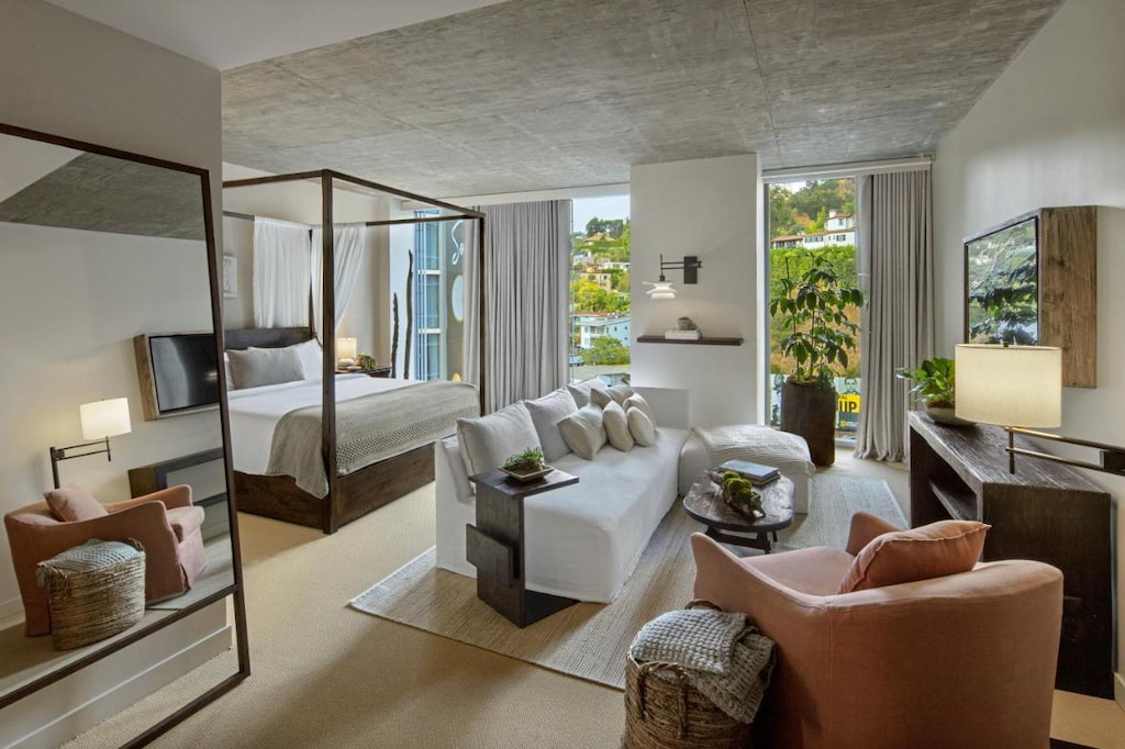 A chic hotel in West Hollywood with a living room with white sofa, mirror, bed and a balcony.
