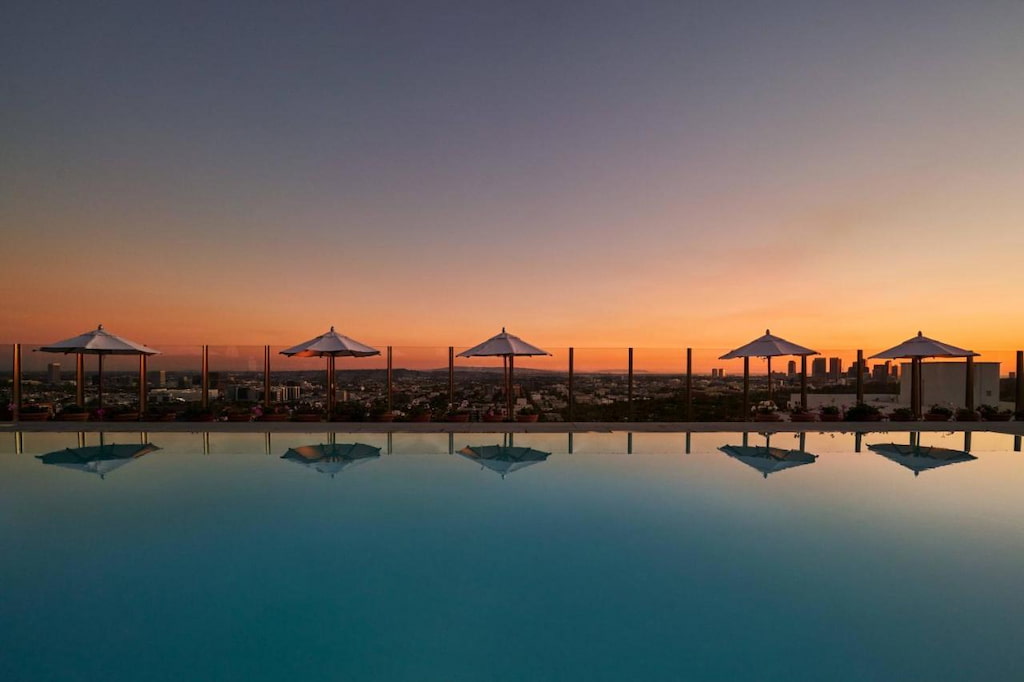 A rooftop pool surrounded by pool benches and umbrellas at sunset.