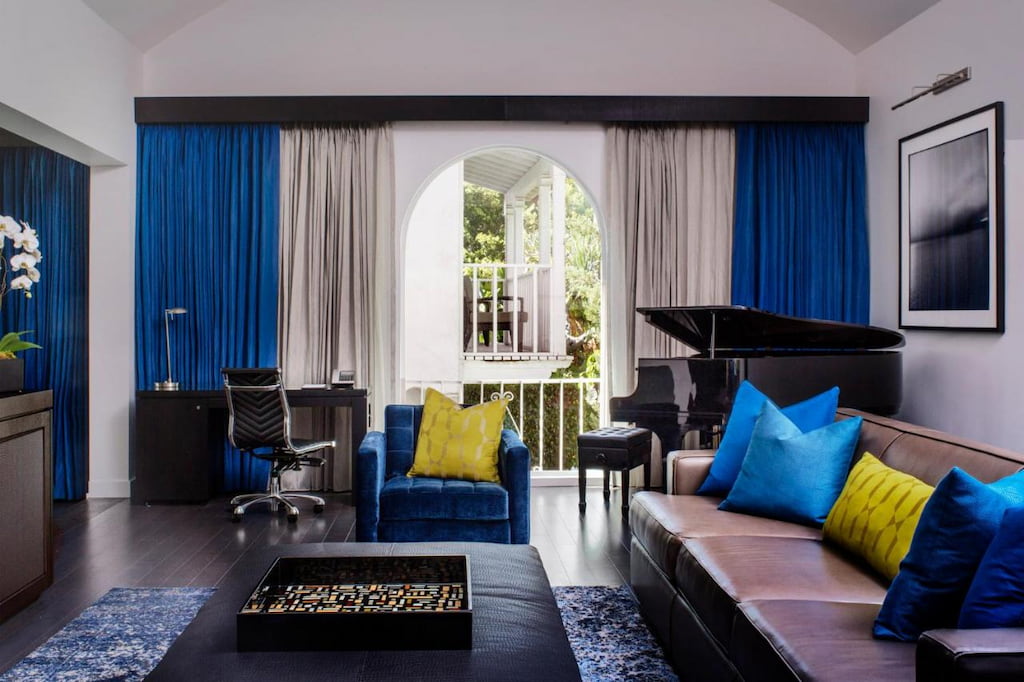 An elegant living room at one of the coolest hotels in WeHo California with modern tables and chairs, blue, black and yellow decor and piano near the balcony.