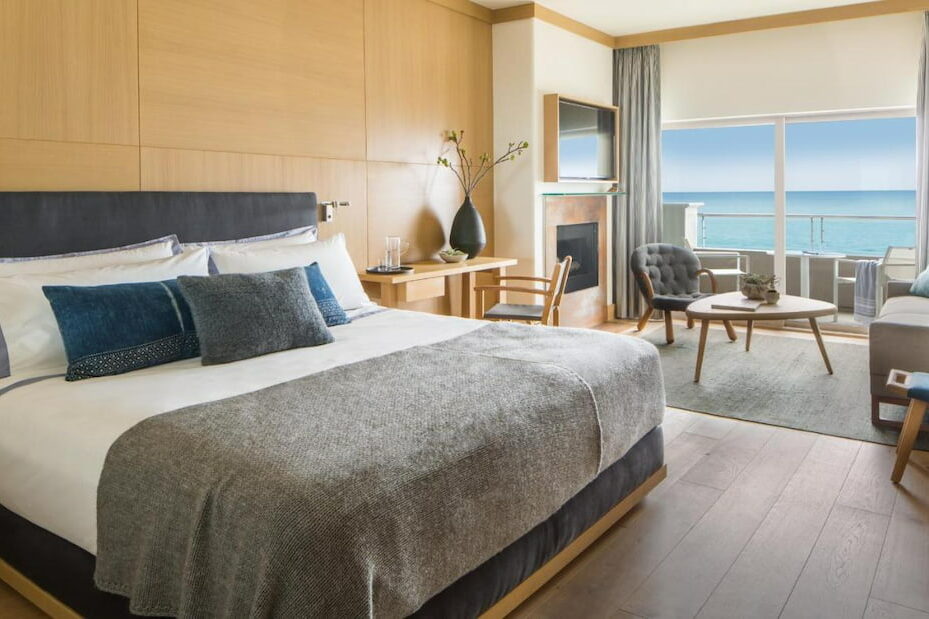 View of a luxury boutique hotel in Malibu California with a cozy king size bed, tables and chairs and a balcony.