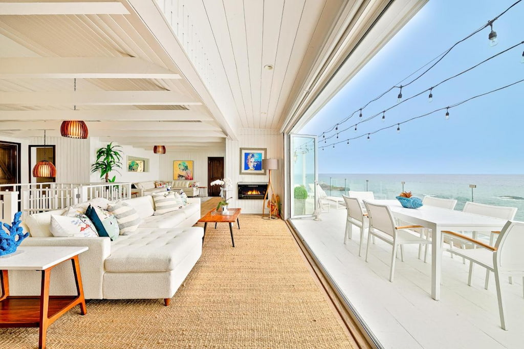 A chic living room at a beachfront hotel in Malibu CA with white couch facing the beach near the balcony with tables and chairs.