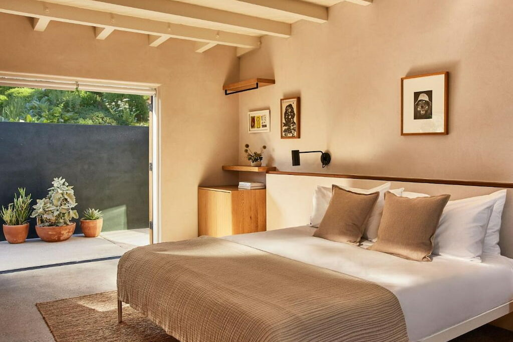A cozy Malibu hotel room with a comfy bed with white sheets near the potted plants.