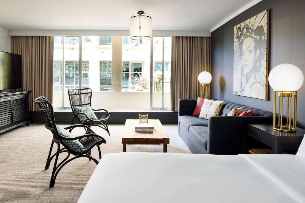 San Francisco boutique hotel suite area with black couch, black wicker accent chairs below a painting on a black wall with a balcony in the distance.