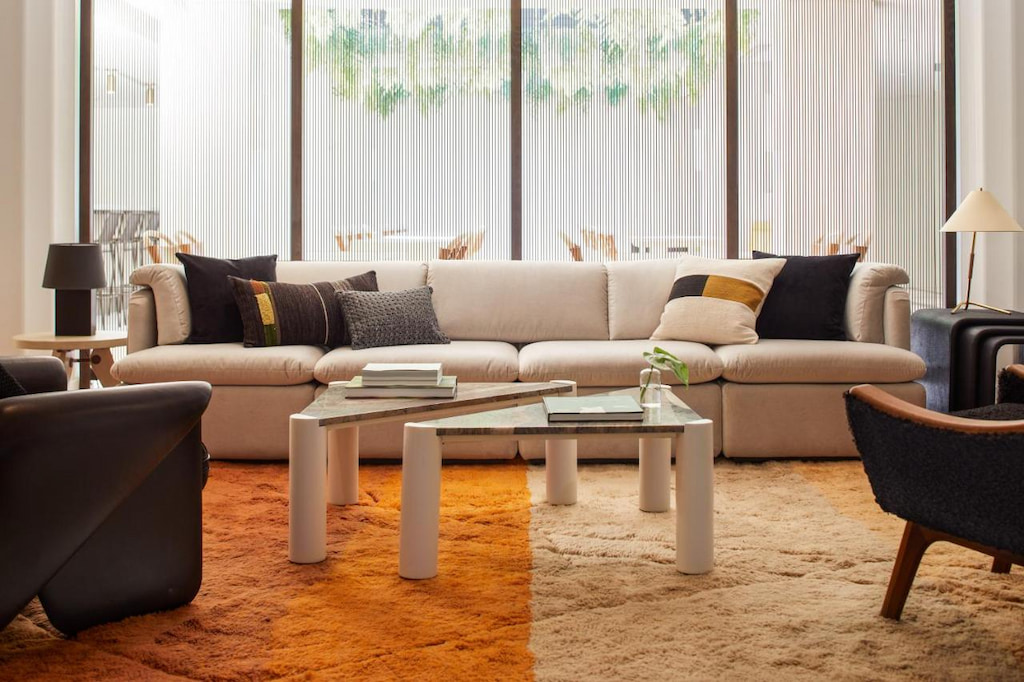living room area with a long creme colored sofa by the window and an orange rug