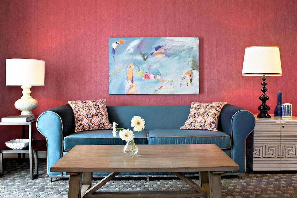 hotel suite area with a plush blue sofa in front of the wooden table and red wall
