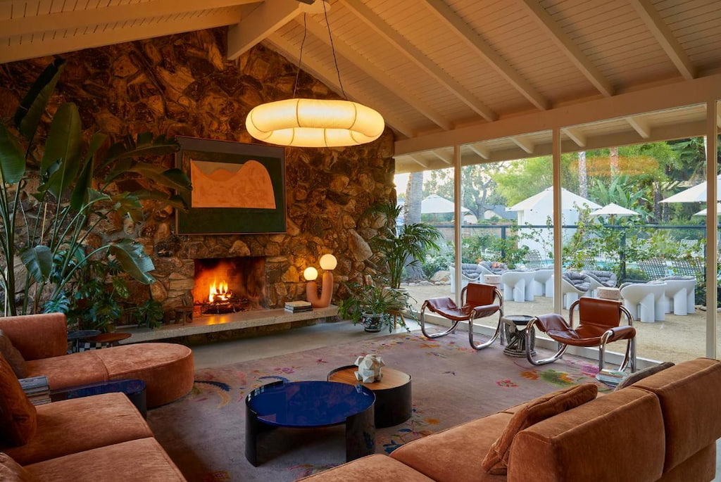 earthy colored furnishings infront of a wood burning stone fireplace with floor to ceiling windows in a boutique hotel