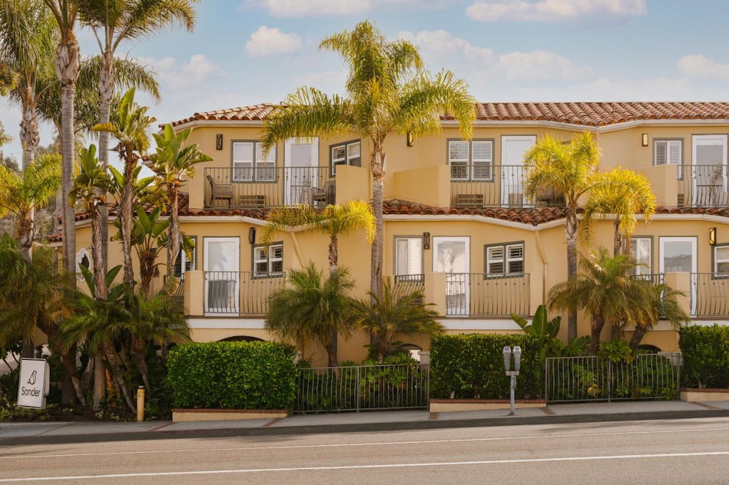 Exterior view of the Sonder in a Californian style architecture with light yellow colored facade, green hedges and palm trees in front of a paved road