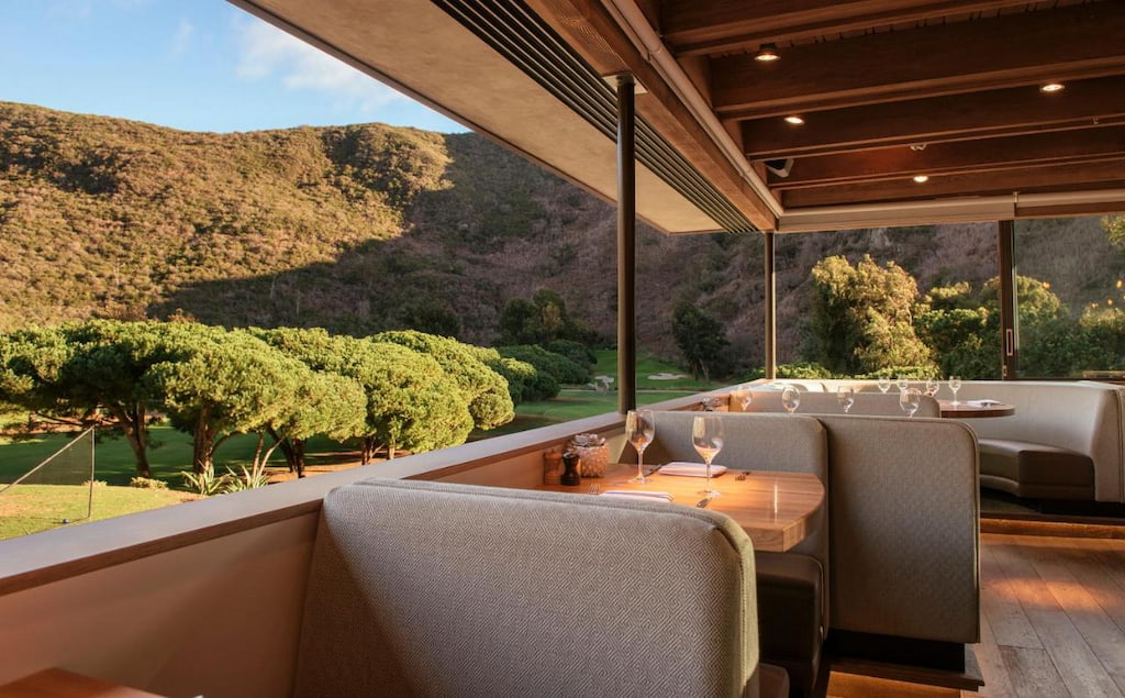 onsite restaurant with plush grey bench seating, and an outdoor view of the rolling green hills in the distance