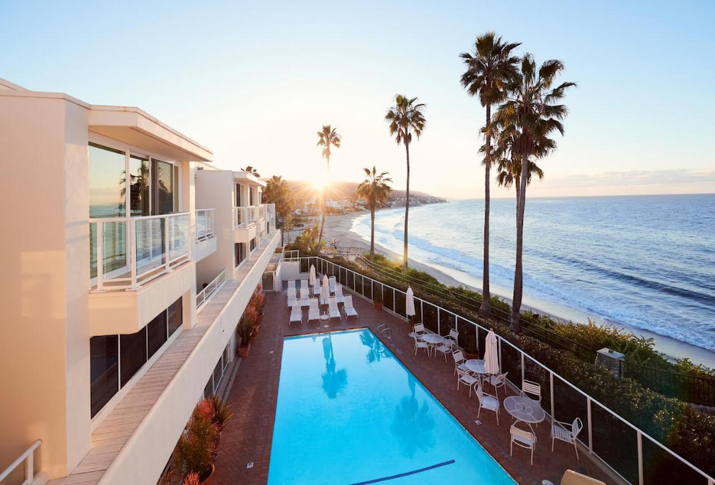beachfront hotel in Laguna Beach with its outdoor pool near tall palm trees and ocean in the background