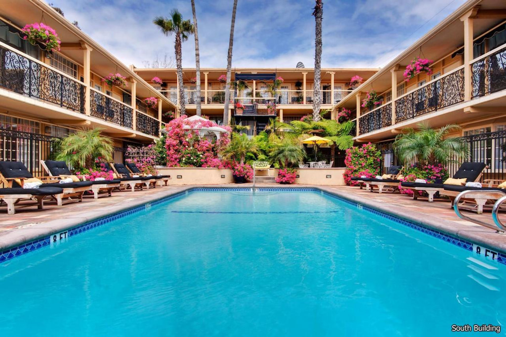 outdoor pool surrounded by a 2 story Laguna Beach hotel on three sides with green and pink foliage and black cushioned sun loungers