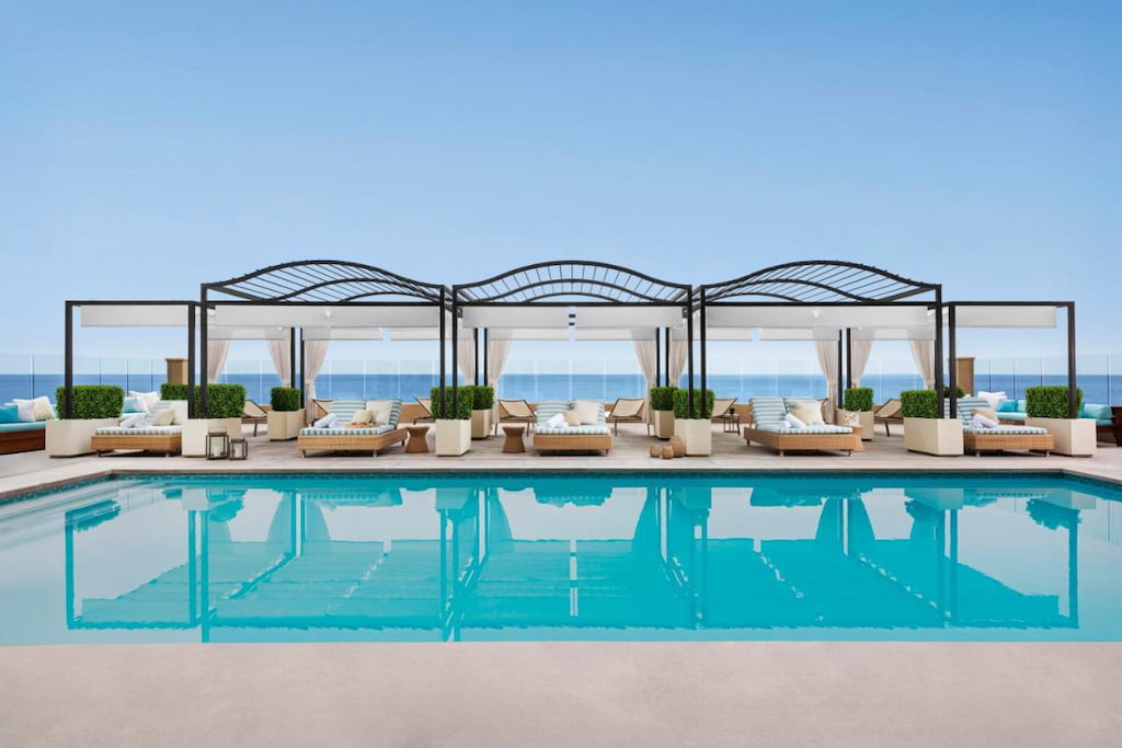 outdoor pool with reflection of sun loungers with canopy on the water on a clear blue sky day in California