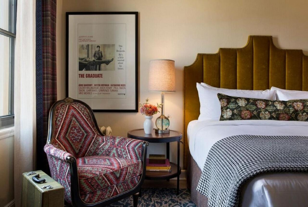 A bedroom in one of the boutique hotels in Berkeley with a carpeted floor, double bed, chair, floor-to-ceiling curtain, and circular bedside table