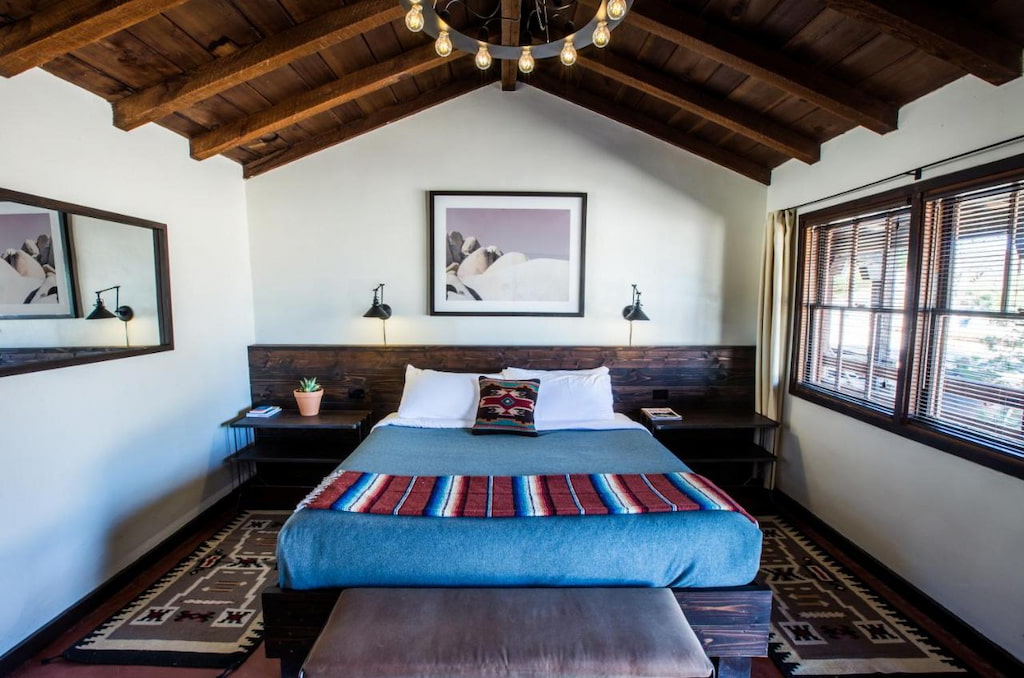 cozy bed with blue sheets and a wood clad ceiling and window near Joshua Tree NP