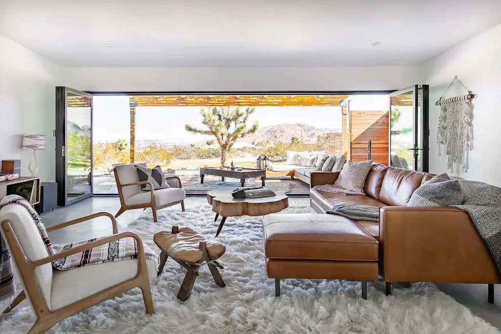 living room with low lying ceiling and brown leather couch in front of the wooden center table with Joshua Tree desert in the background