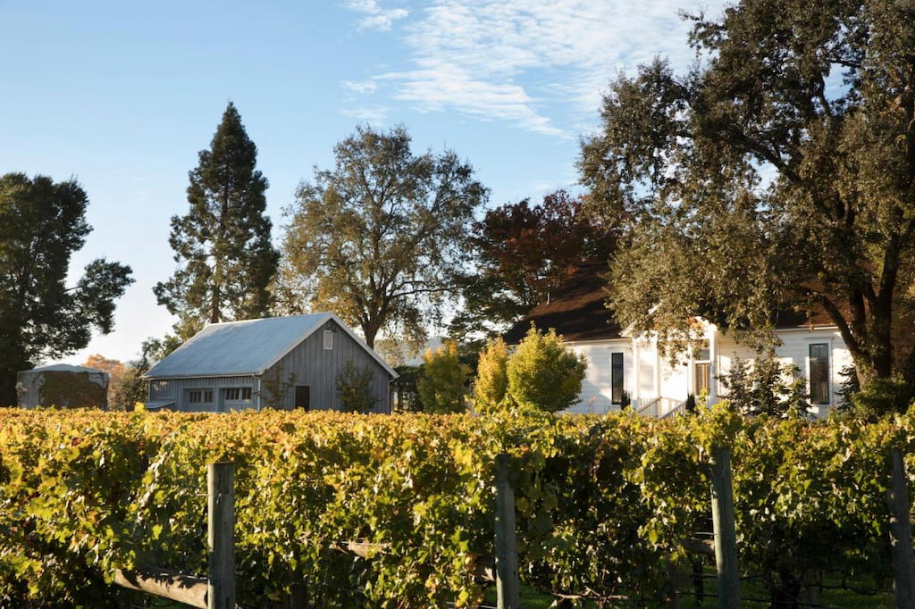 Exterior view of a Napa Valley boutique hotel with white paint surrounded by vineyards and trees under a blue sky.
