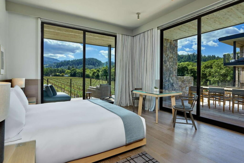 a romantic hotel in Napa with a ceiling-to-floor windows and view of the fields outside the hotel with a cozy bed with white sheets