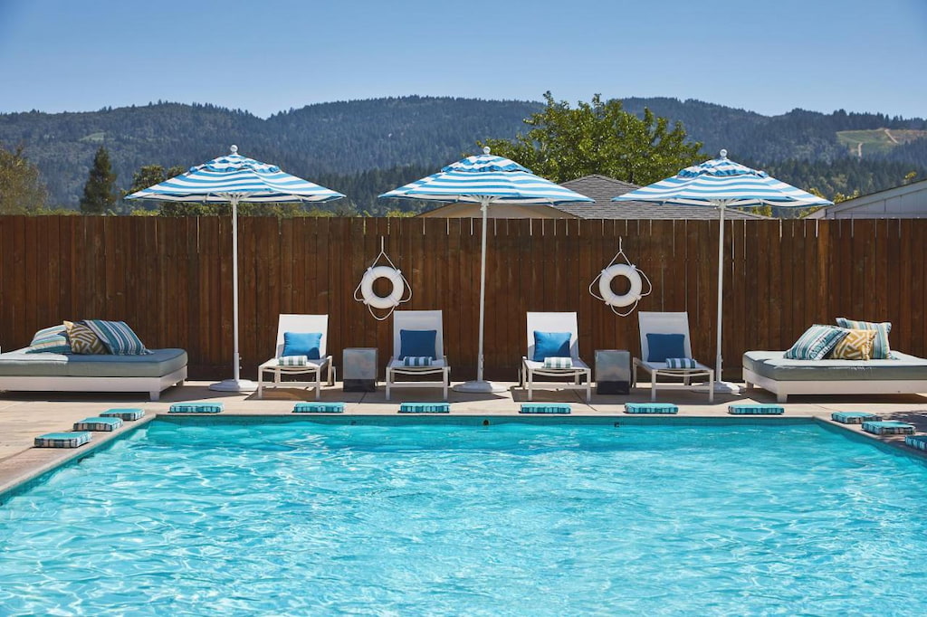 pool area surrounded by pool benches and striped umbrellas and mountains at the background under a clear blue sky