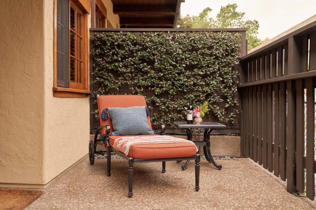 A small outdoor patio area with a lounger chair with orange foam beside the wall near the fence