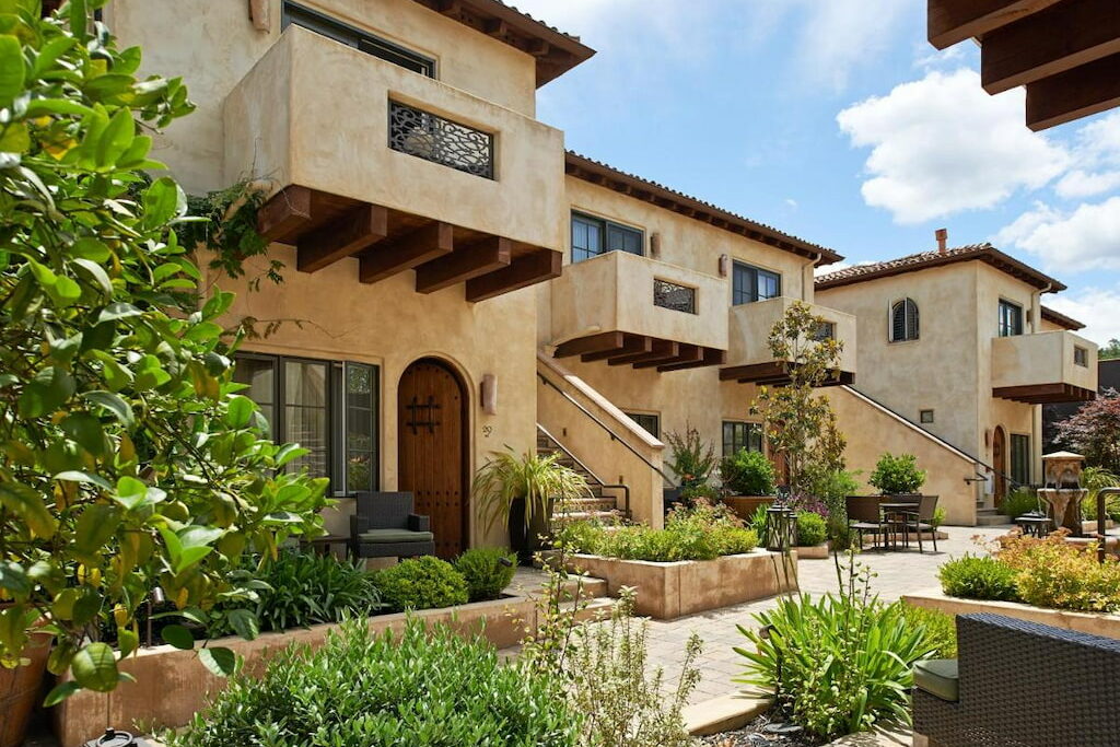 sandstone sided Napa hotel with arched wooden door and balconies surrounded by greenery under a sunny sky