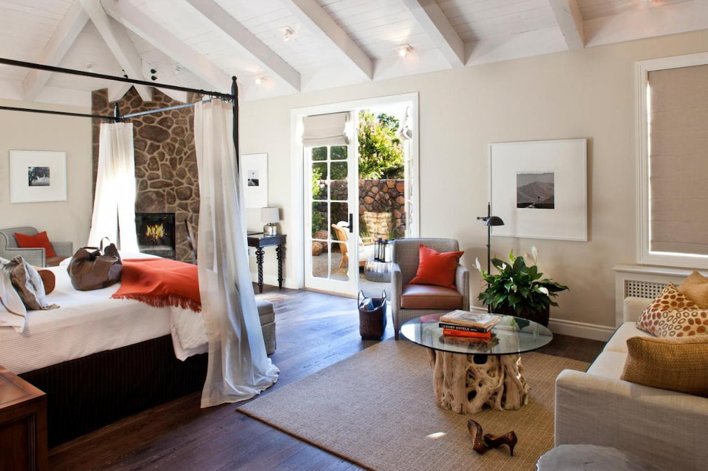 a luxury hotel in Napa Valley with a bed with metal frame near the round table with glass top beside the white couch.
