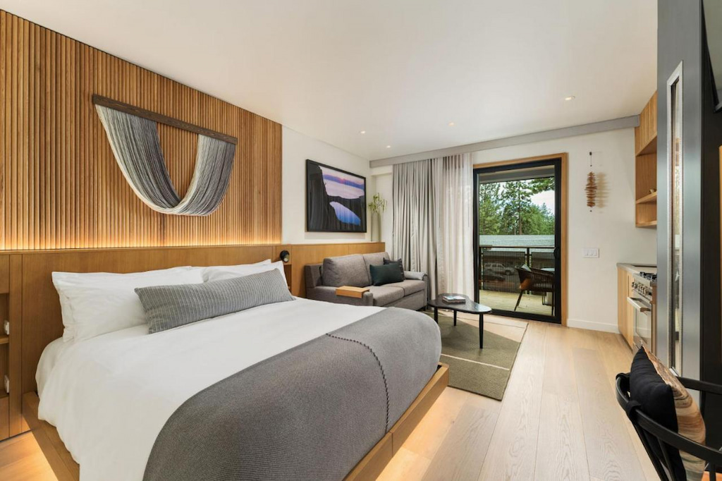 modern hotel suite with grey and white linens on a king sized bed, wood slat feature wall with couch in the distance