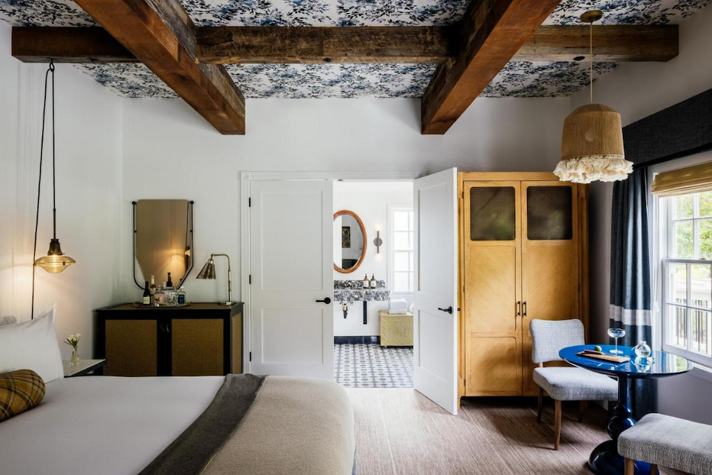 historic hotel suite with wood dresser and beams on a patterned ceiling with bathroom in the distance