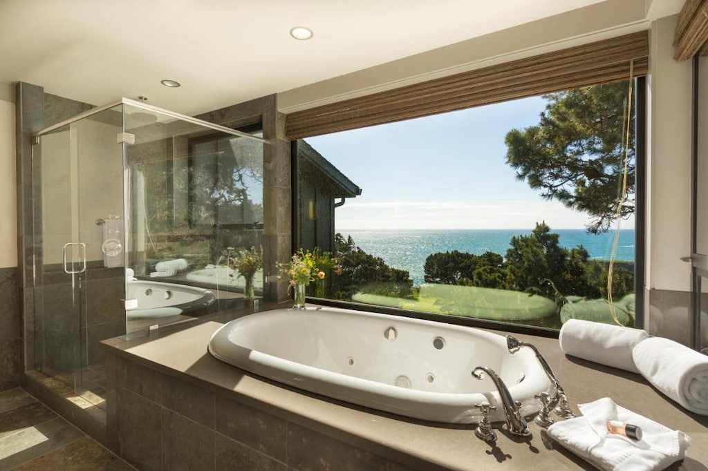 bathroom with a built-in bathtub and a glass shower area with an ocean view through a window
