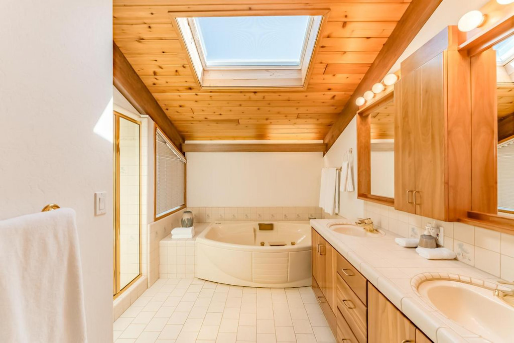 bathroom with a built-in bathtub, long double sink vanity, and a skylight on a wood slated ceiling