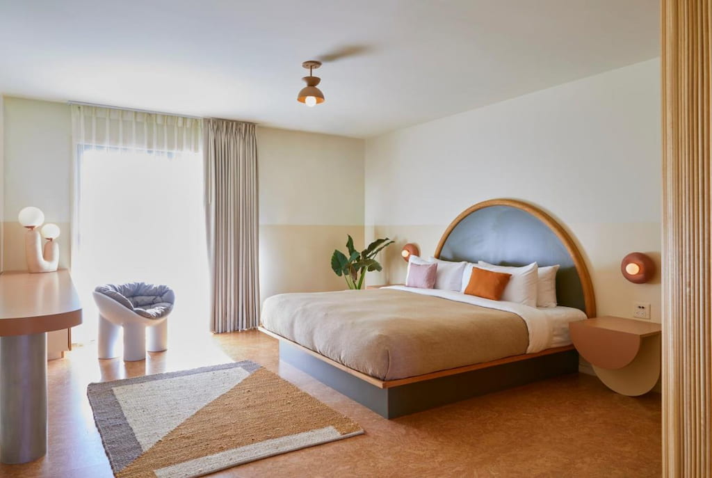 A spacious bedroom with a cozy bed, accent chair, and a potted plant in the corner in one of the Ojai boutique hotels.