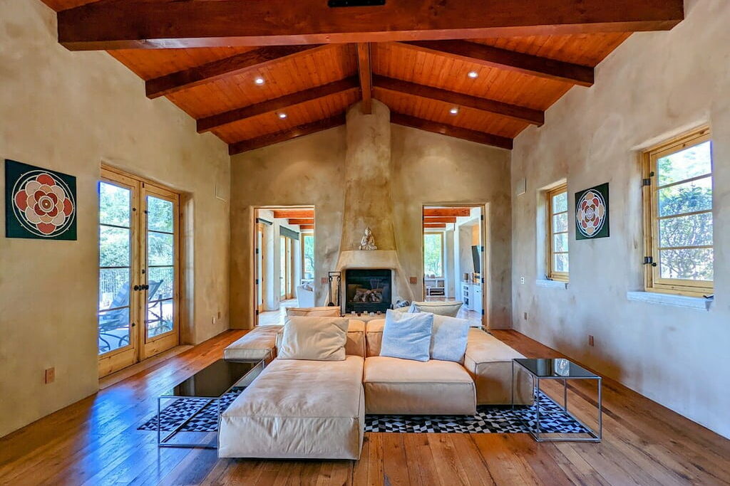 A Ojai Valley hotel suite with a large creme colored selectional couch and stone fireplace under a wood ceiling.