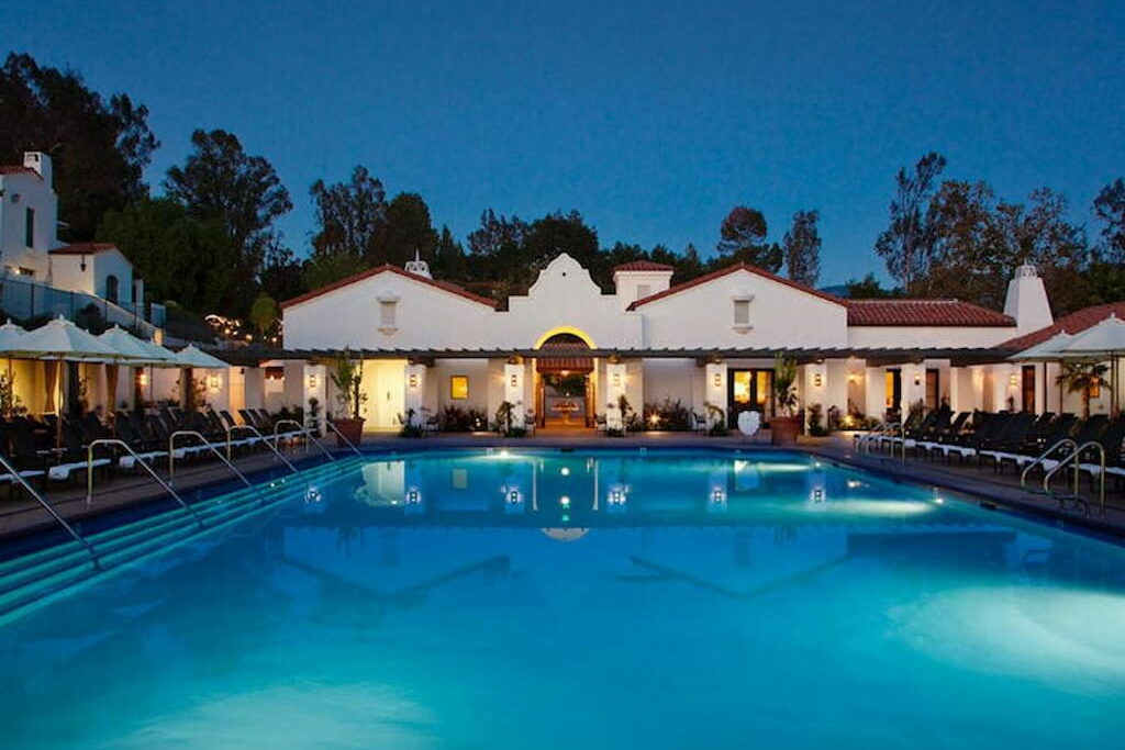 An outdoor swimming pool in front of a hacienda style accommodation surrounded by padded pool benches at night in one of the Ojai hotels.