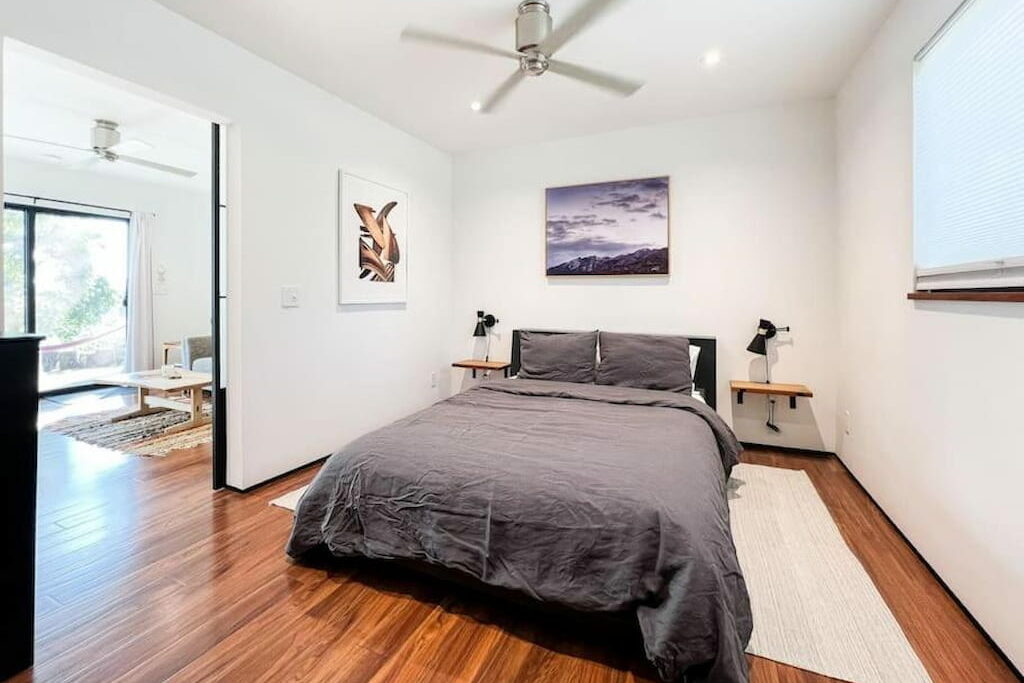 A spacious bedroom with. abed with gray sheets below a ceiling fan.